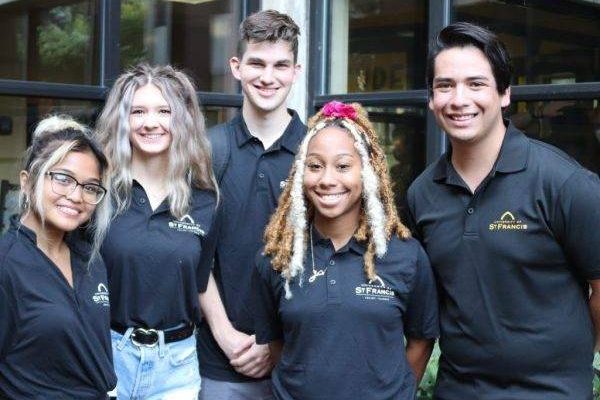 students smiling together wearing university of saint francis shirts